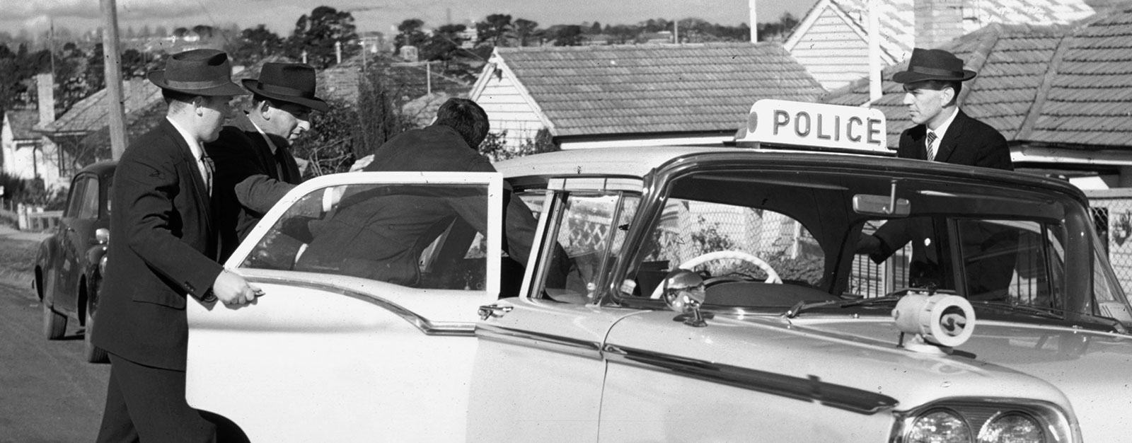 Photo of detectives putting a suspect in a police car